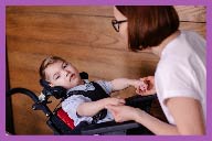 Woman and child embracing as child sits in assistive chair