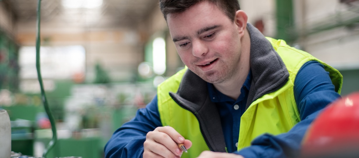 Man in green high vis vest with Down Syndrome working on assembly line